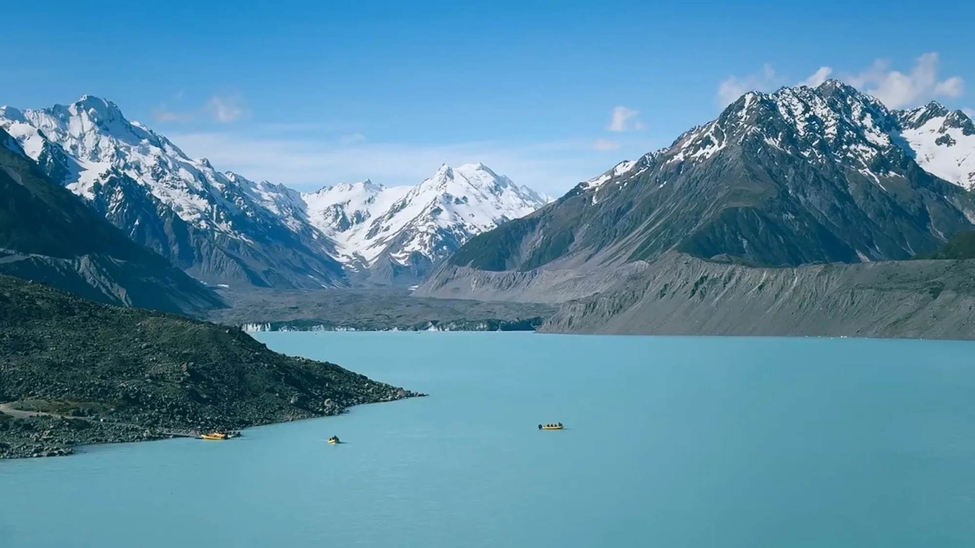 Small boats crossing the turquoise Tasman Glacier Lake