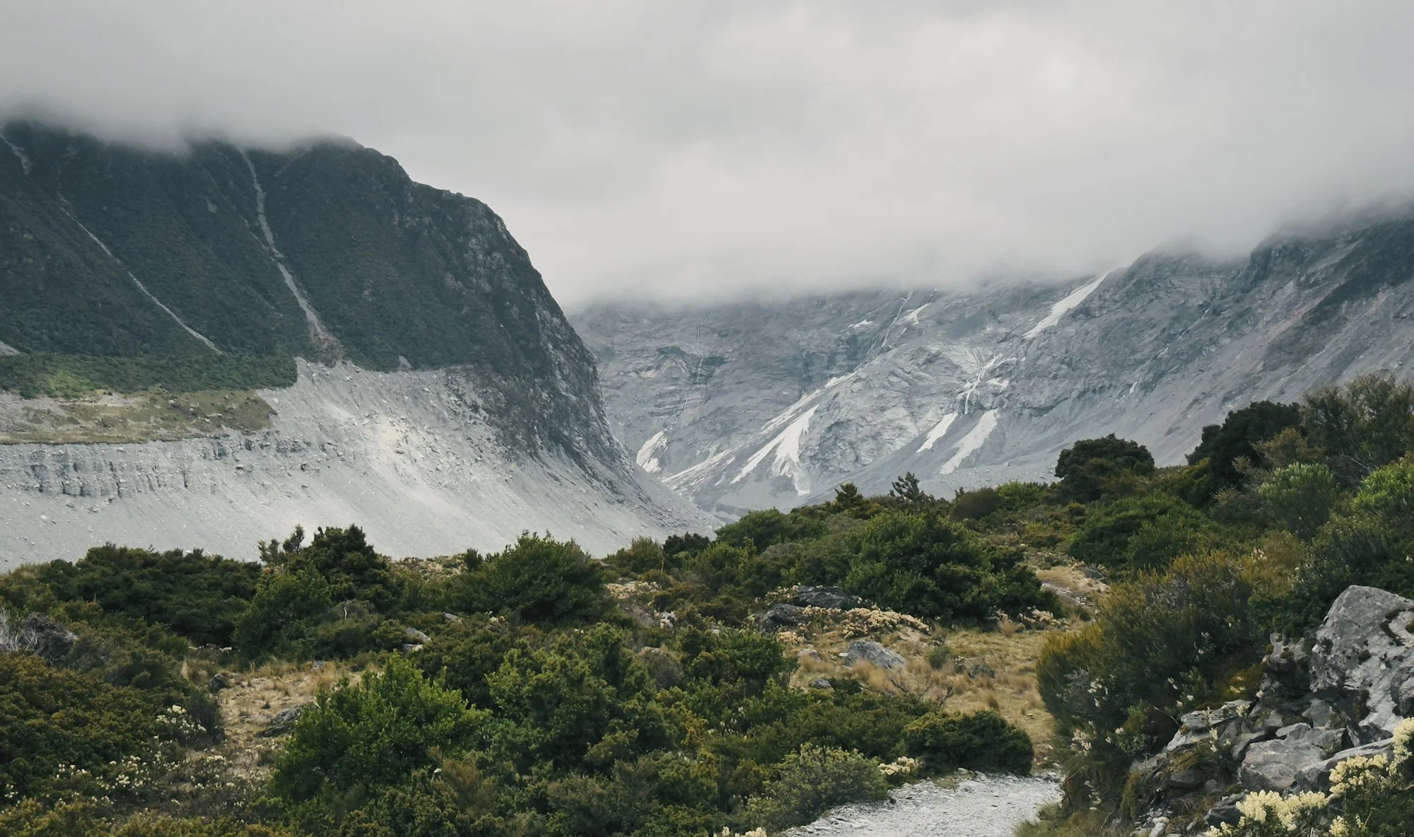 The Hooker Valley Track winding between misty mountain walls
