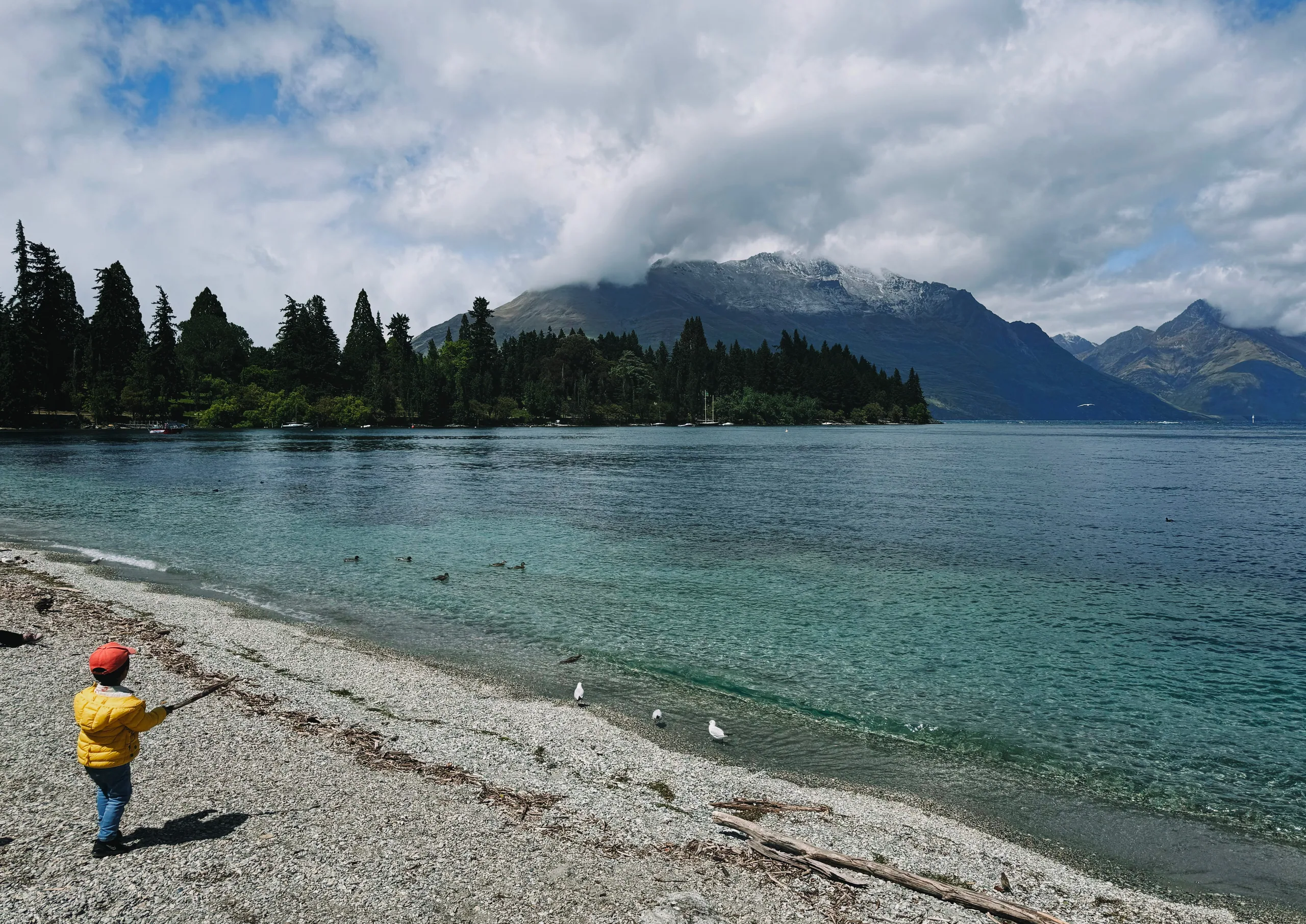 The stony Lake Wakatipu shore beneath cloud-covered mountains