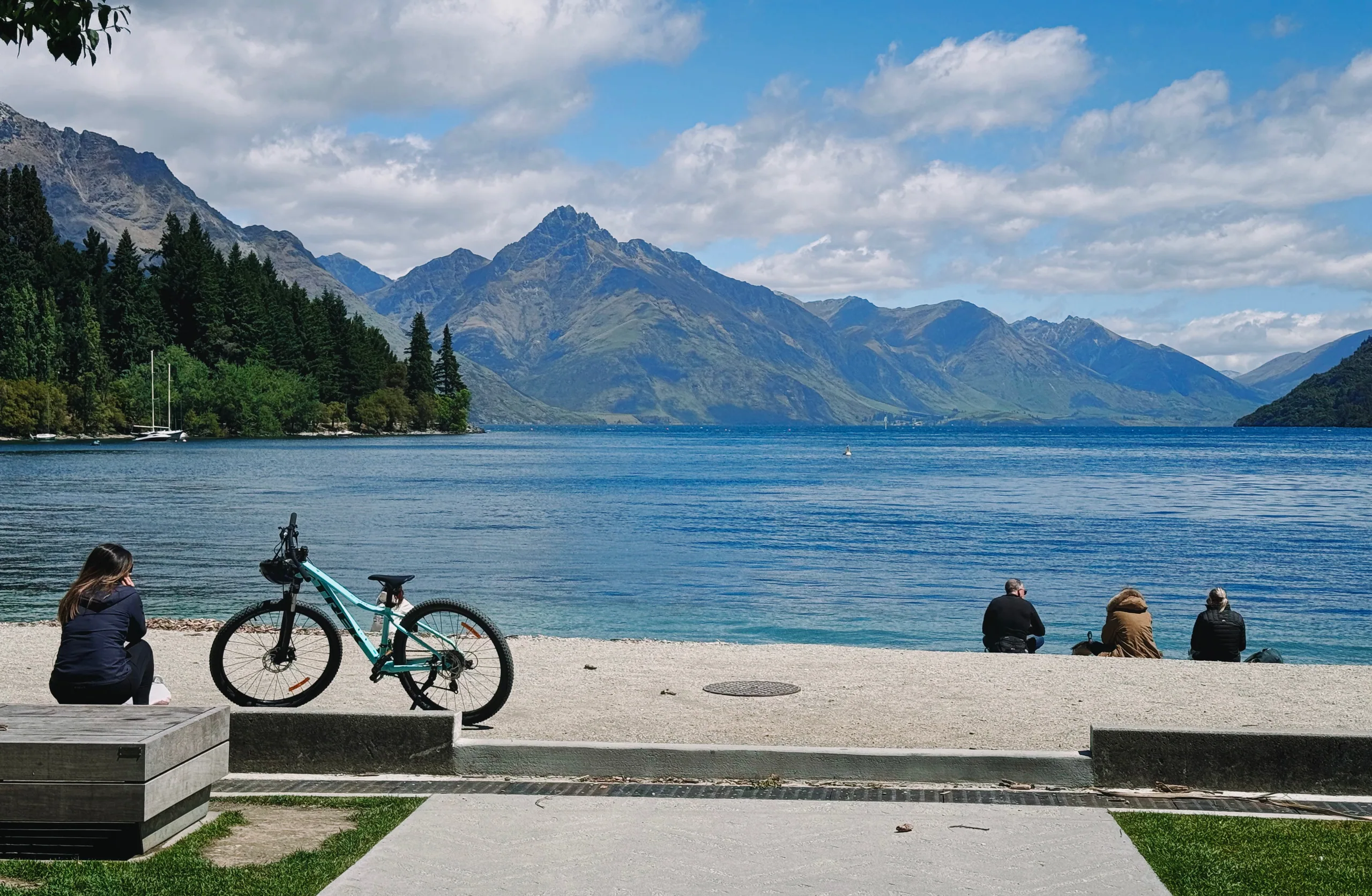 A bicycle and visitors on Queenstown's lakeside promenade
