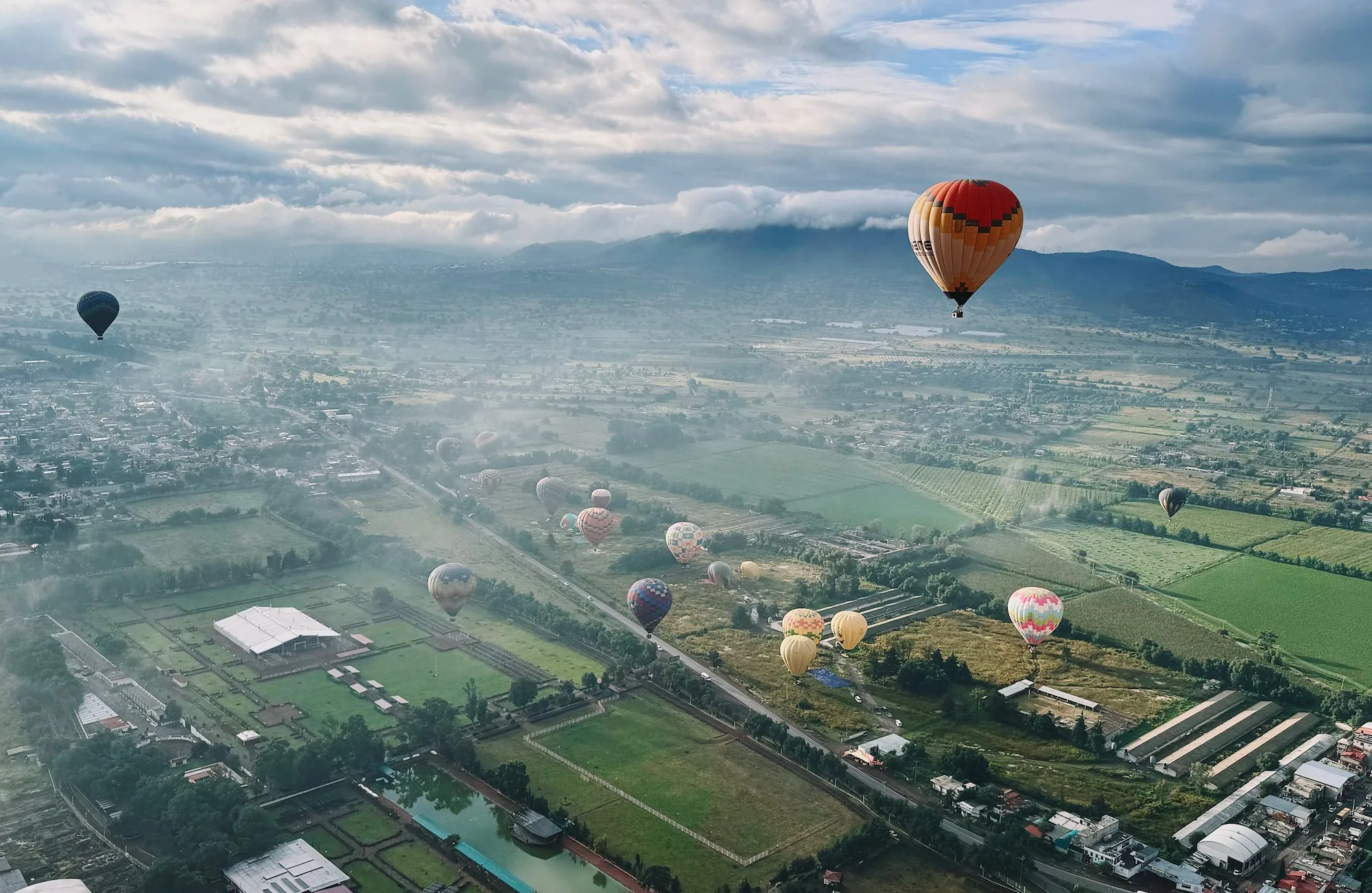 Balloons descending over fields in light morning fog