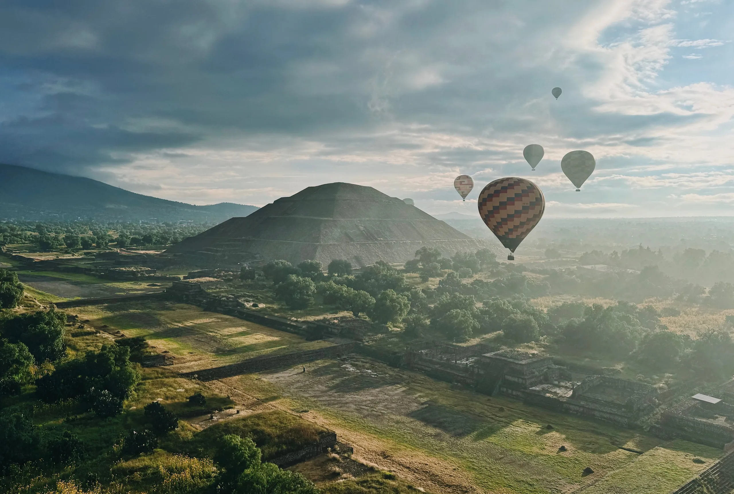 Hot air balloons drifting over the pyramids of Teotihuacan at dawn